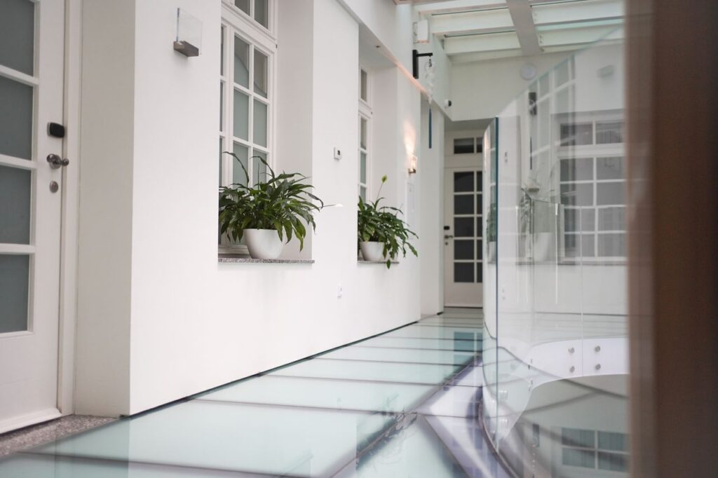 pexels-photo-11433148-11433148 Sleek interior hallway with glass floor and plants, featuring clean and minimalist design.